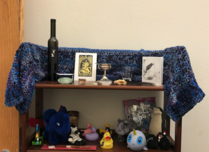 The top shelf of a bookcase, decorated with various objects and an image of Odin. The shelf below it contains a variety of plushie animals.