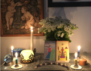 An altar with several lit candles, a bunch of white flowers, and two images of the Goddess Persephone.