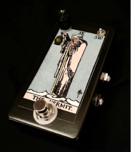 A black-framed guitar pedal with the Rider-Waite-Smith Hermit figure on it.