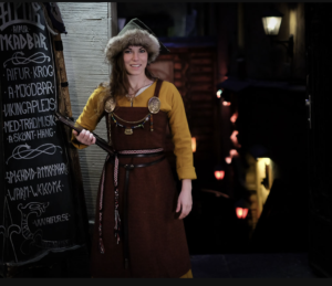 A woman in a Viking apron dress with elaborate jewelry stands in the door of the restaurant.