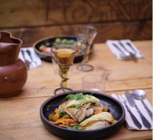 A photo of the feast table, with plates of food, a glass set in an iron stand, and a pottery pitcher.