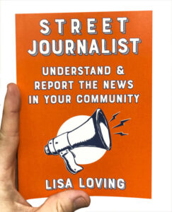 A photo of a hand holding a copy of Lisa Loving's book titled Street Journalist.