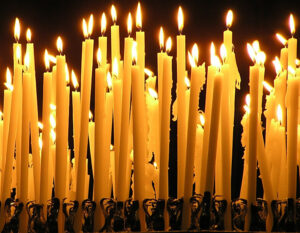 A photo of many candles of varying heights, lit and softly glowing.