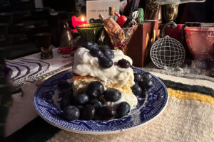 A photo of a small plate which holds a piece of sponge cake covered in blueberries and whipped cream.